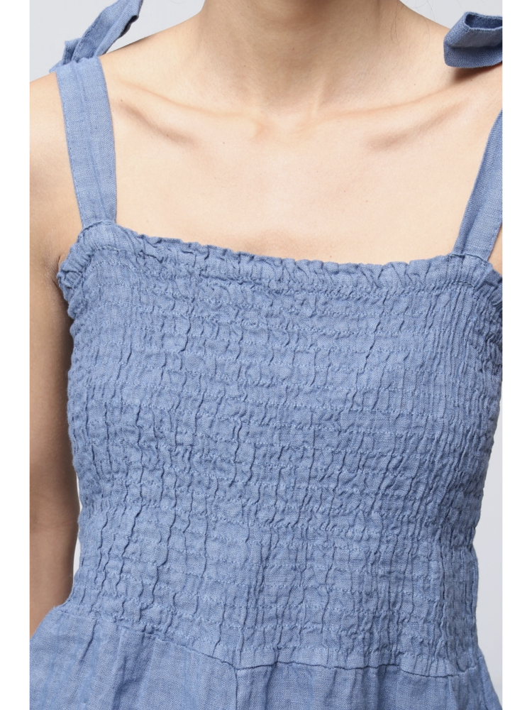 Woman wearing a jeans blue 100% linen jumpsuit with a smocked bodice, tie-shoulder straps, and wide-leg trousers.
