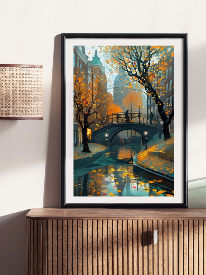 A framed art print depicting an autumn canal scene with orange trees, a bridge, and reflections in the water, displayed on a wooden cabinet against a light wall.