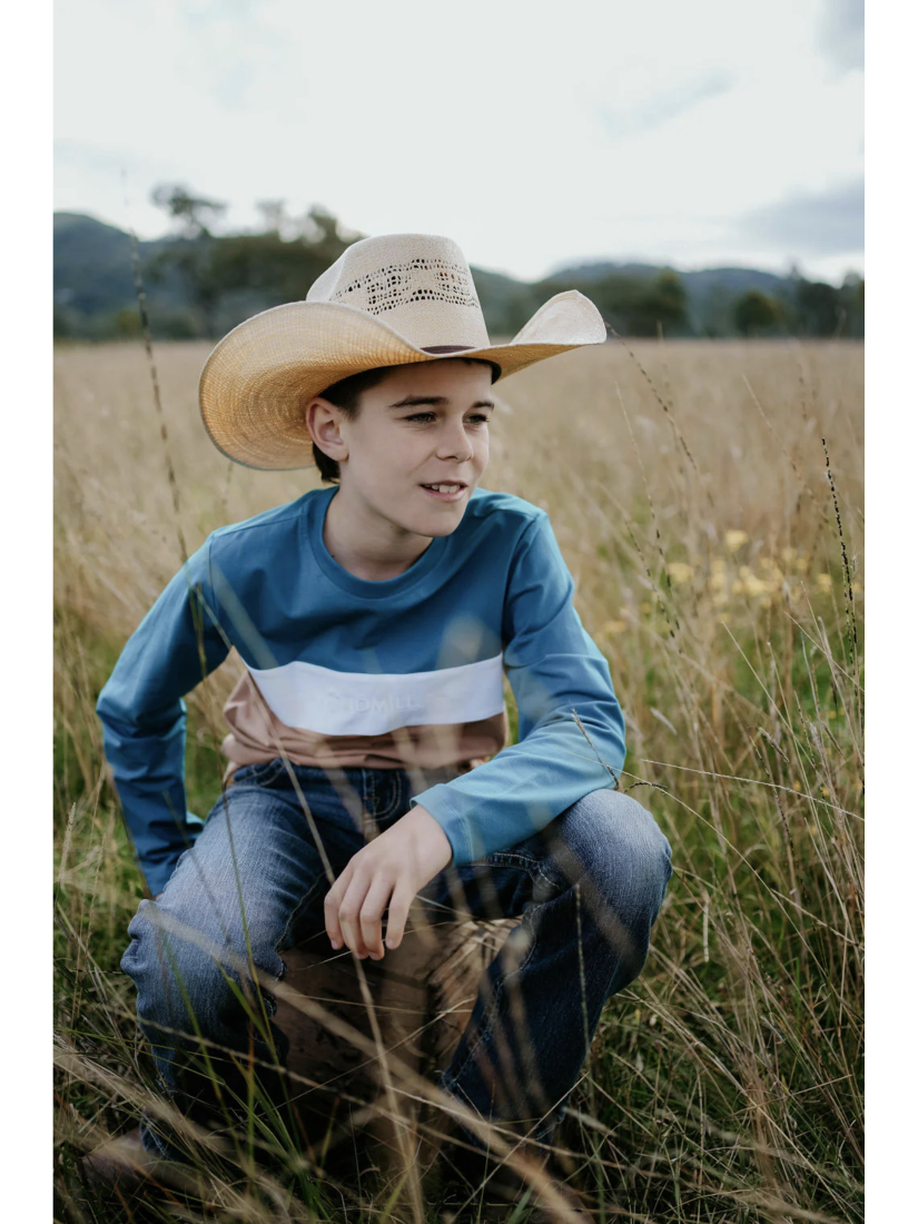 Young boy wearing a cowboy hat and colorful shirt sitting in a field.