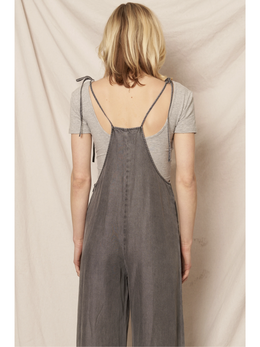 Black soft denim jumpsuit featuring adjustable tie shoulder straps, a square neckline, and a breezy wide-leg silhouette on a model.