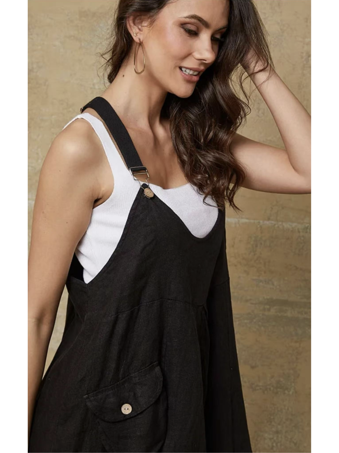 Model in a black 100% linen jumpsuit with a relaxed fit, adjustable buckle straps, and button details at the ankles, over a white tank top.