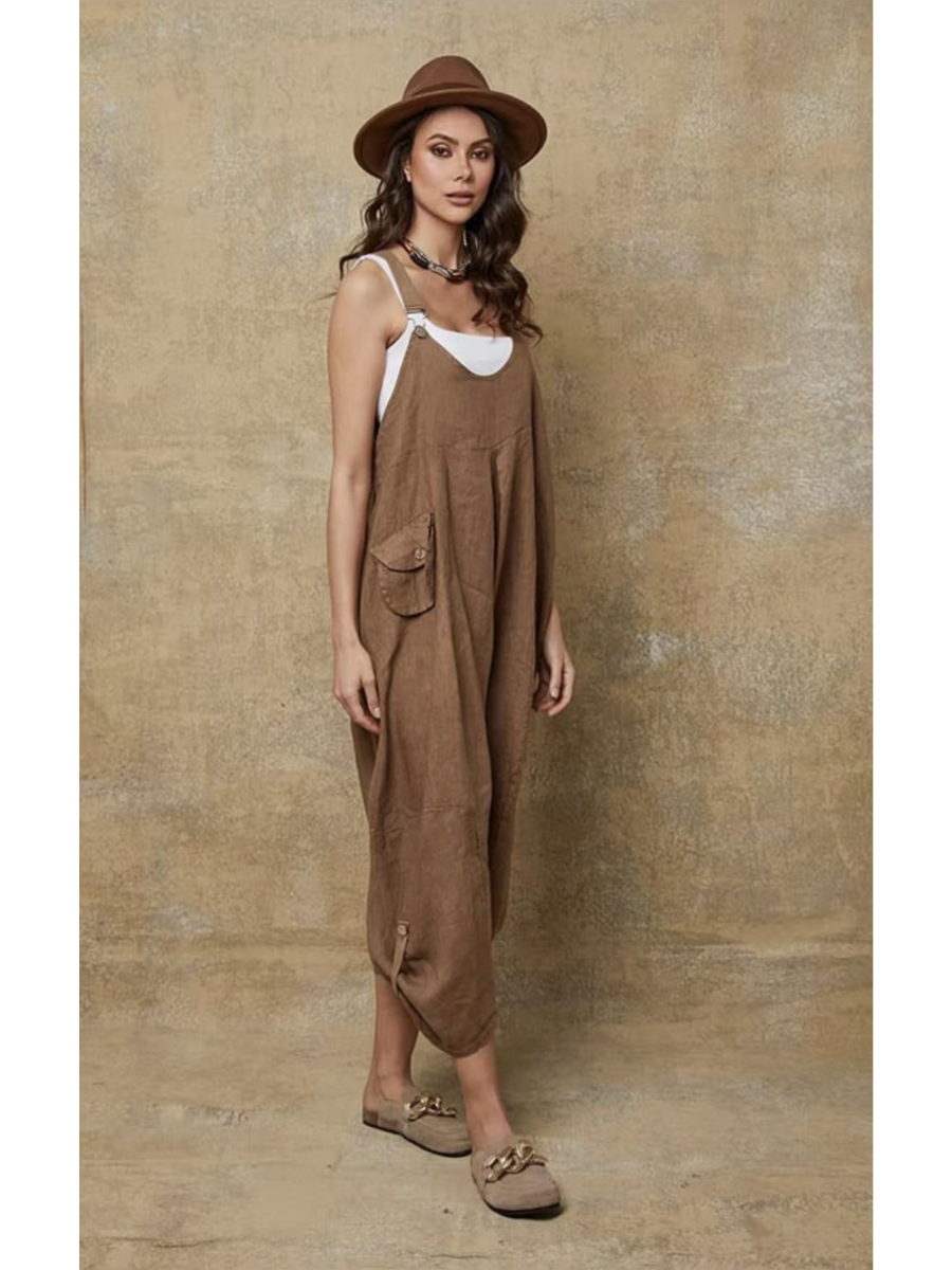 Model in a camel 100% linen jumpsuit with a relaxed fit, adjustable buckle straps, and button details at the ankles, over a white tank top.