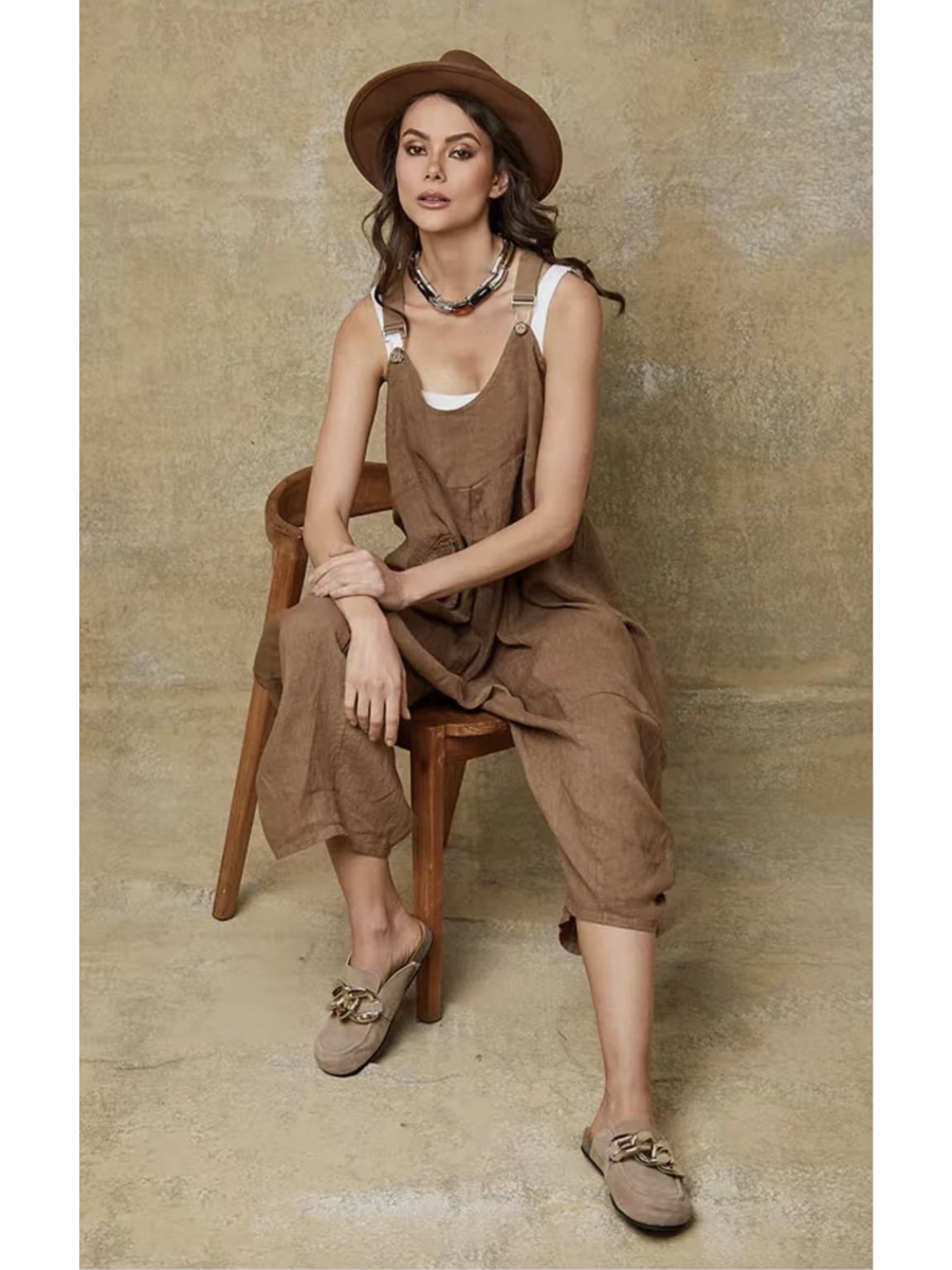 Model in a camel 100% linen jumpsuit with a relaxed fit, adjustable buckle straps, and button details at the ankles, over a white tank top.
