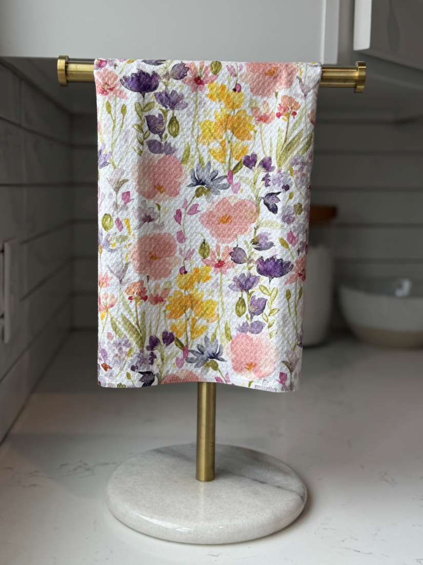 Decorative tea towel featuring a detailed floral print with multiple flowers  on a white background.