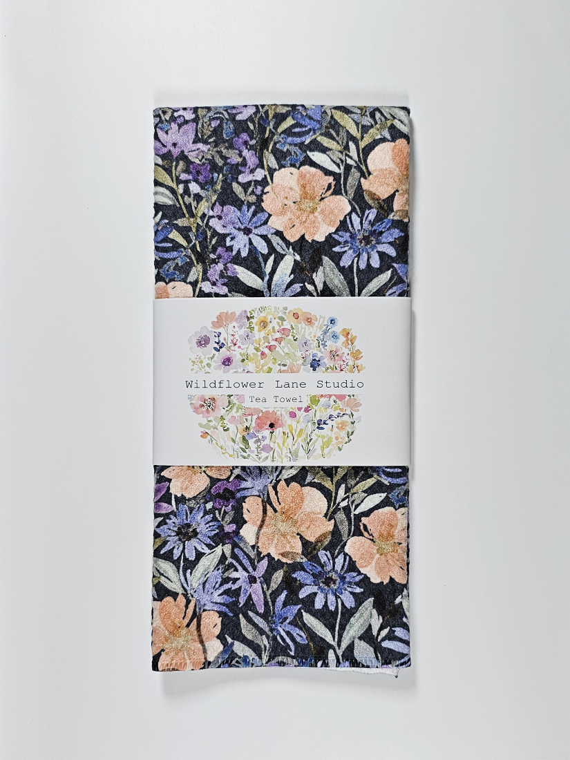 Decorative tea towel featuring a detailed botanical print with peach flowers and purple petals on a dark background.
