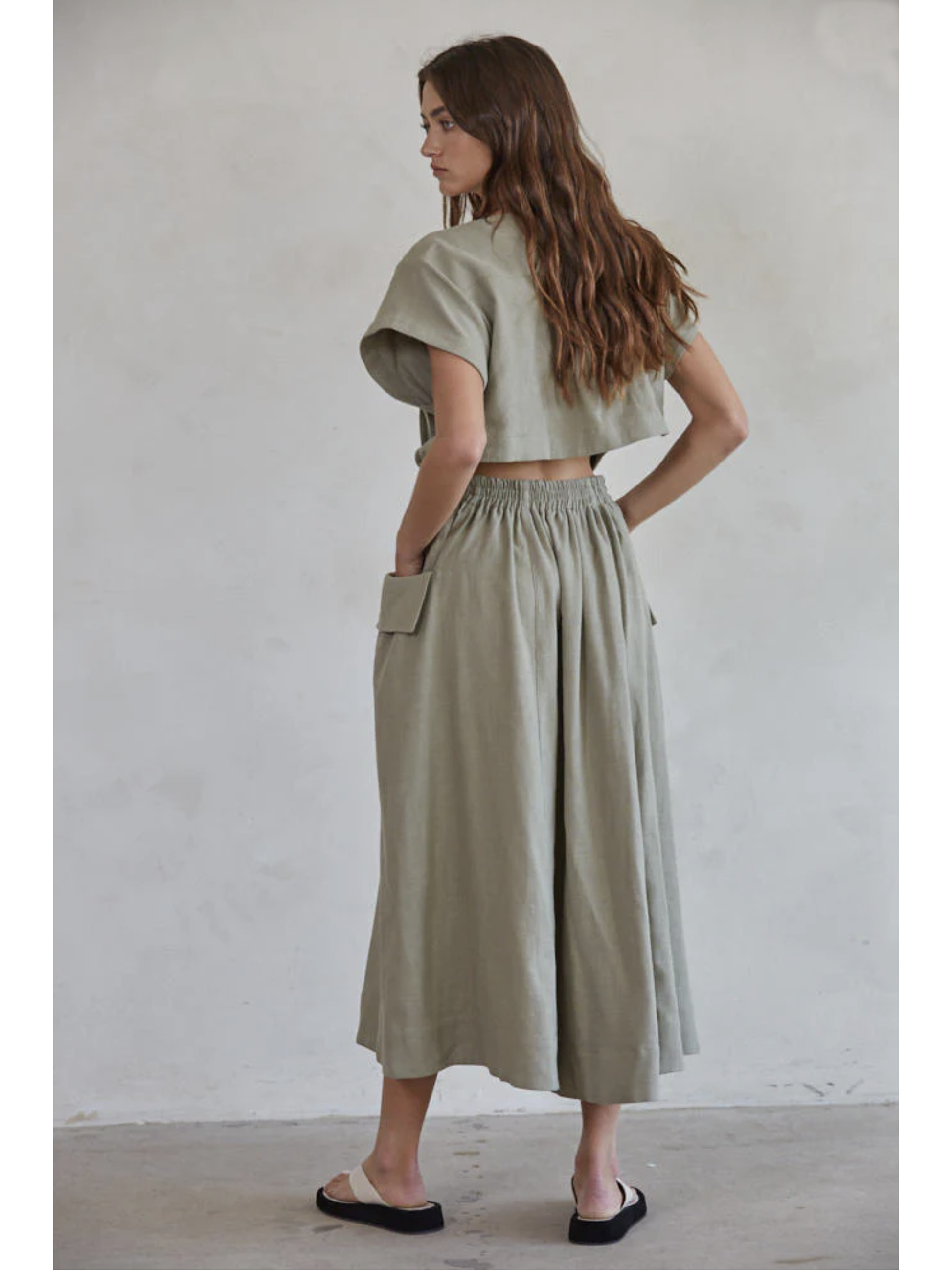 Woman wearing a green outfit with a skirt and top against a plain background