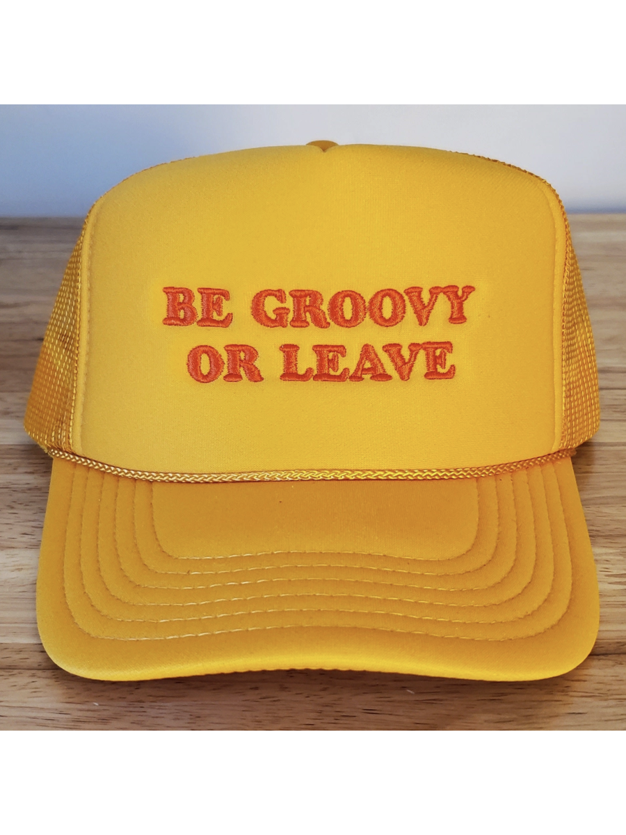 Yellow cap with 'BE GROOVY OR LEAVE' text on a wooden surface