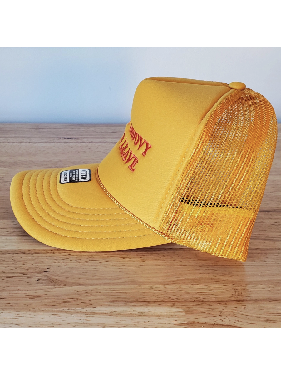 Yellow trucker cap with mesh back showing text 'BE GROOVY OR LEAVE' on a wooden surface