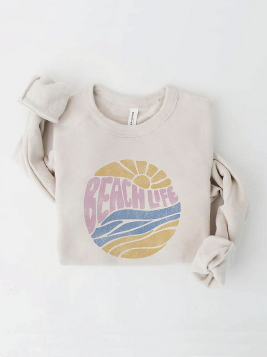 Cream-colored sweatshirt with a circular "Beach Life" graphic featuring a sun and waves in pastel pink, yellow, and blue.