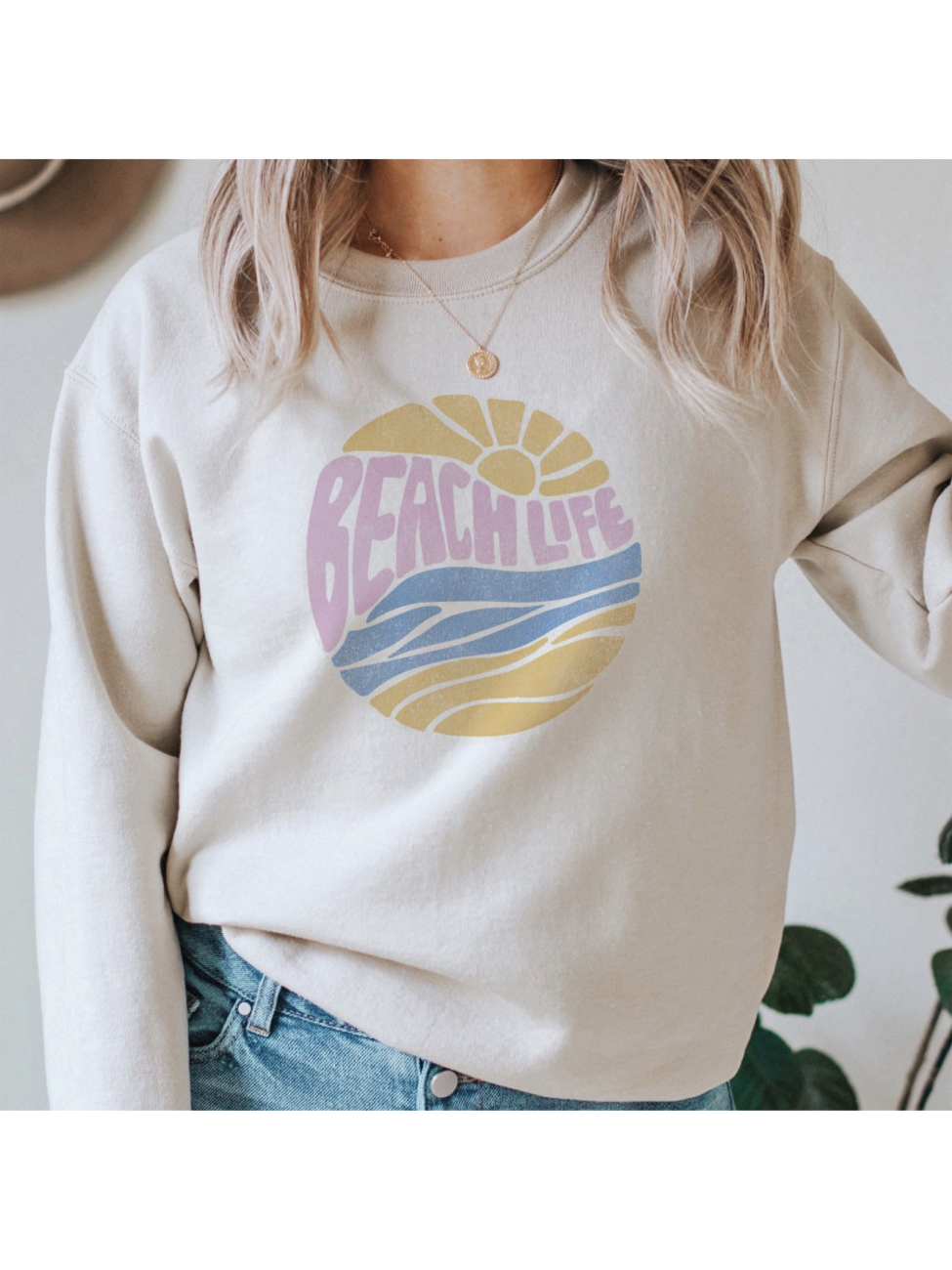 Cream-colored sweatshirt with a circular "Beach Life" graphic featuring a sun and waves in pastel pink, yellow, and blue.