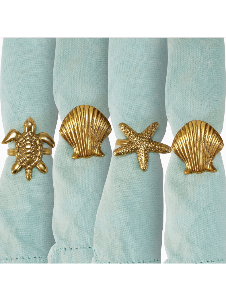 Four gold napkin rings in shapes of a sea turtle, starfish, and seashells holding light blue fabric napkins.