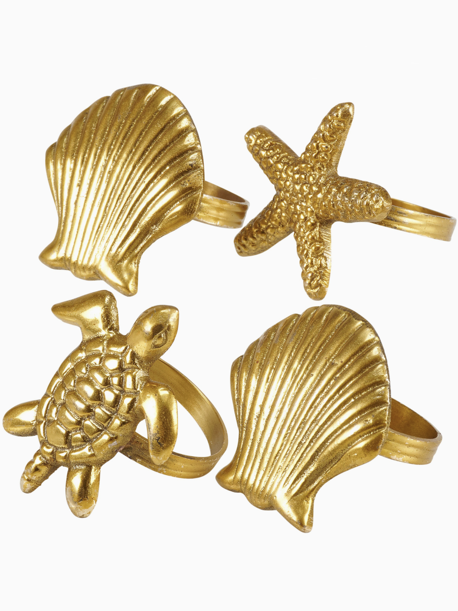 Four gold napkin rings in shapes of a sea turtle, starfish, and seashells holding light blue fabric napkins.