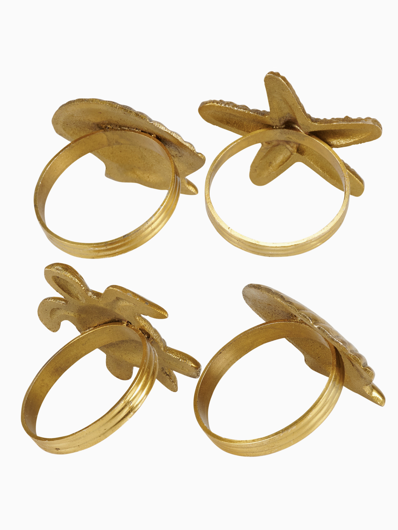 Four gold napkin rings in shapes of a sea turtle, starfish, and seashells holding light blue fabric napkins.