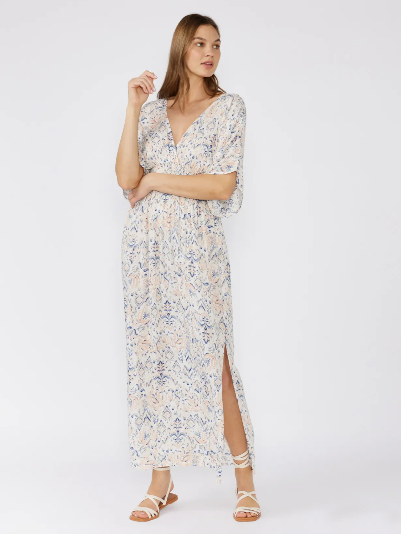 Woman in a white bohemian maxi dress with a blue and peach paisley print, kimono sleeves, and a smocked waist, standing against a white background.