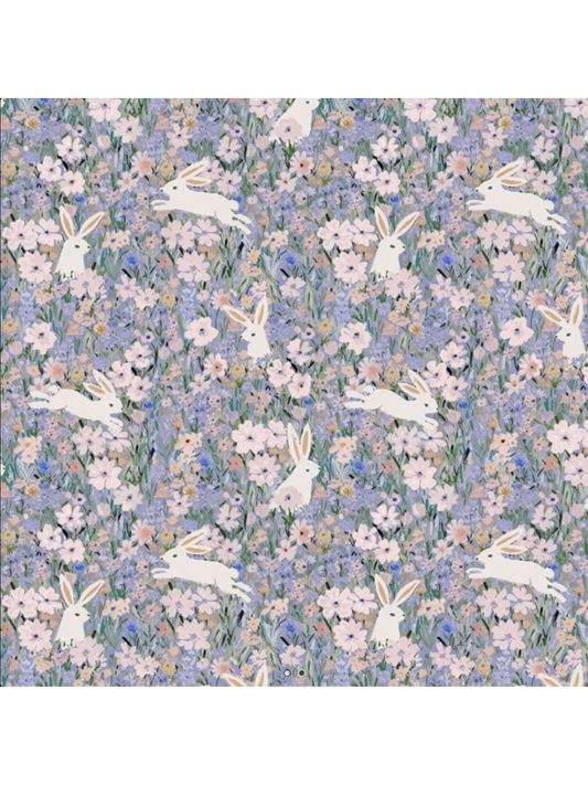 Whimsical fabric pattern with white rabbits leaping through a dense field of purple, pink, and blue watercolor wildflowers.