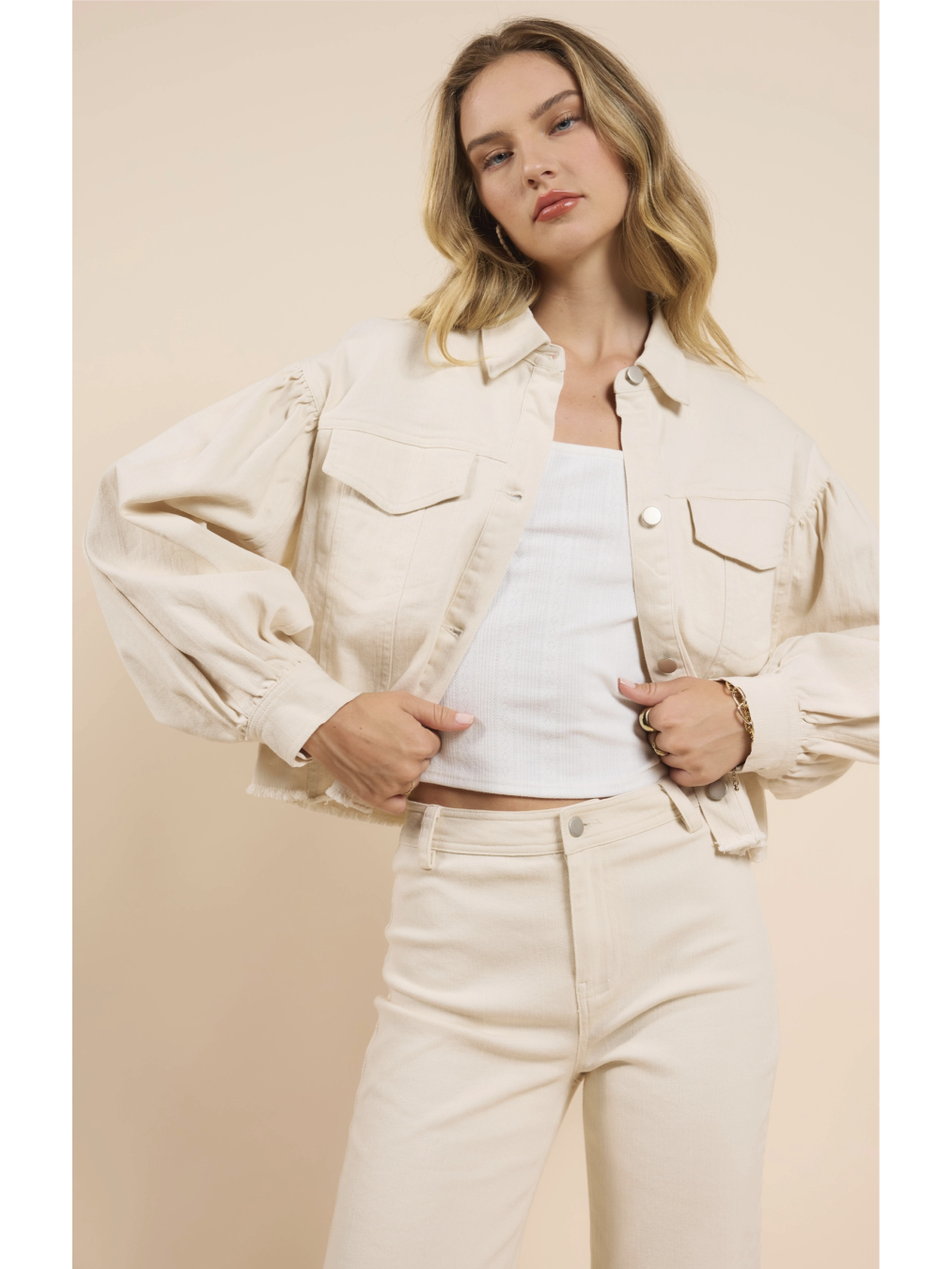 Woman wearing a beige denim jacket over a white top and pants on a beige background