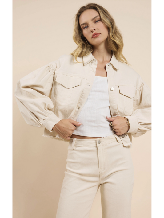Woman wearing a beige denim jacket over a white top and pants on a beige background