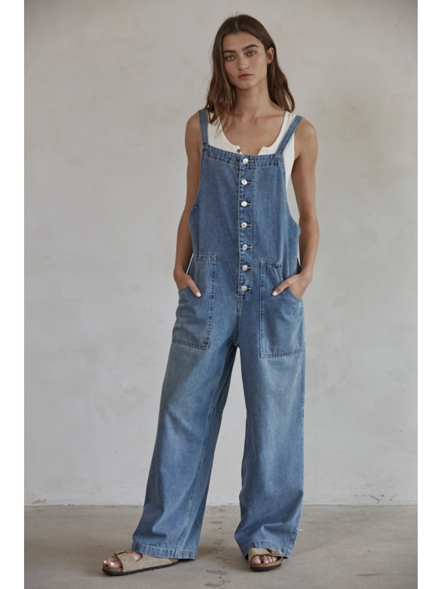 Model in blue denim wide-leg overalls with a square neck and button-down front, styled over a white t-shirt against a plain background.