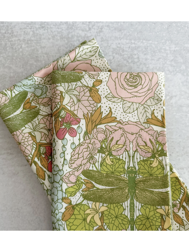Set of four white cloth napkins with a green dragonfly and pink rose watercolor pattern, folded on a light gray surface.