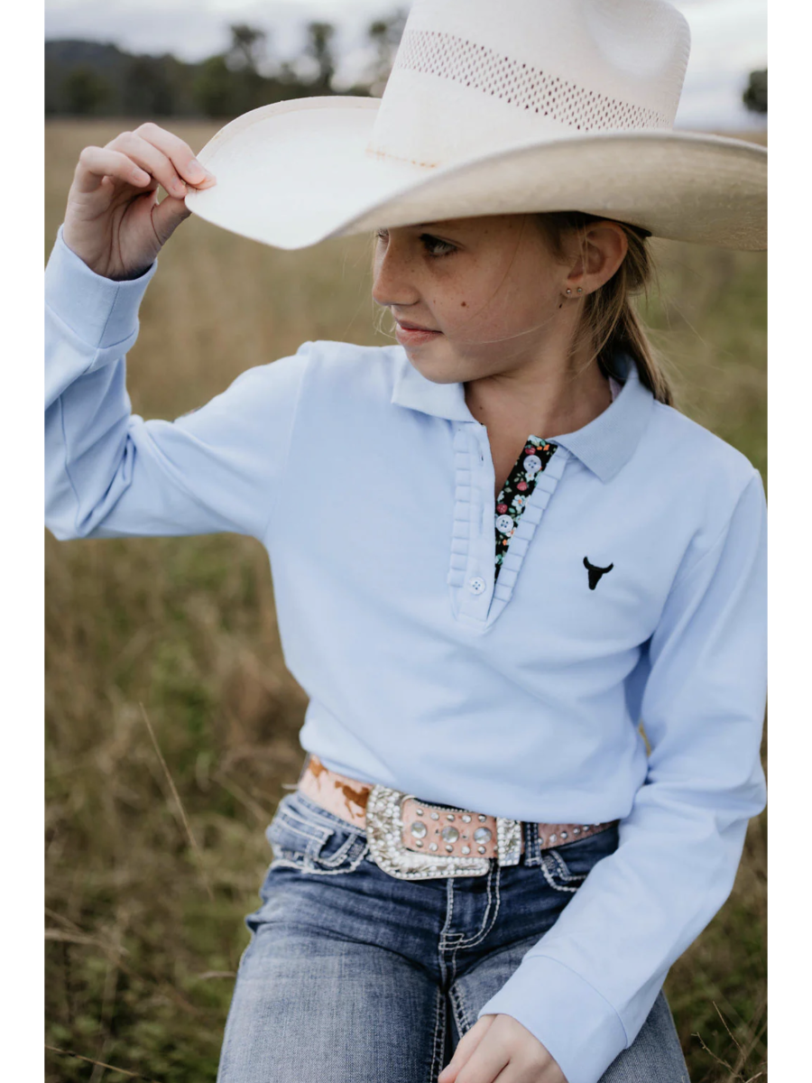 Person wearing a light blue long-sleeve shirt with a logo, jeans, and a cowboy hat in an outdoor setting.