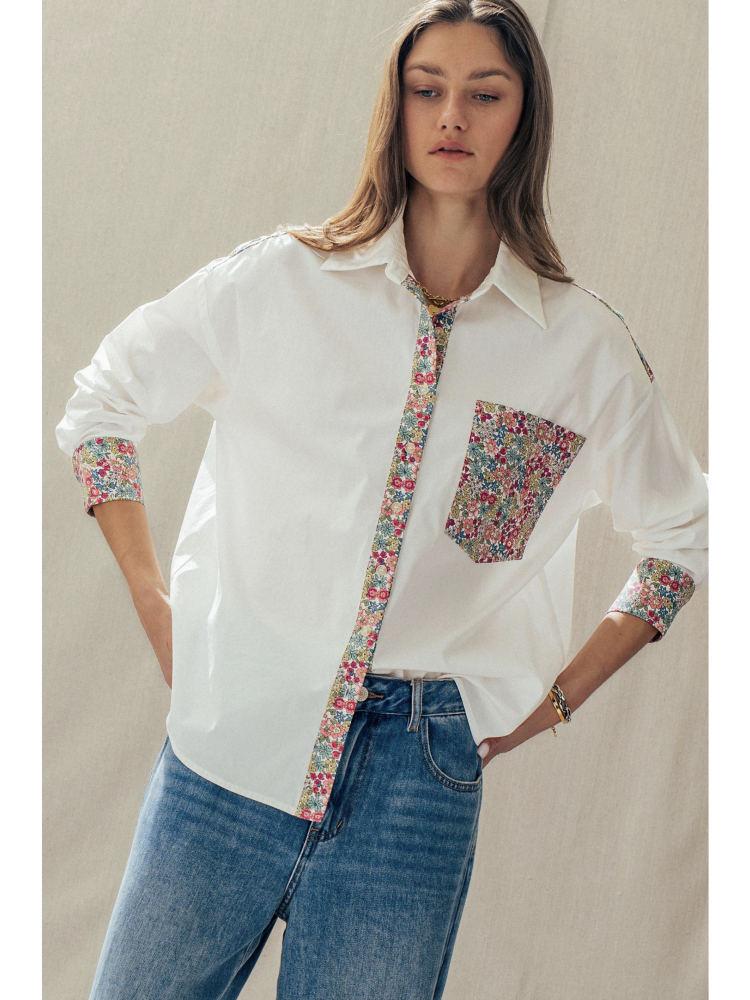 Woman wearing a white shirt with floral trim and pocket on a plain background