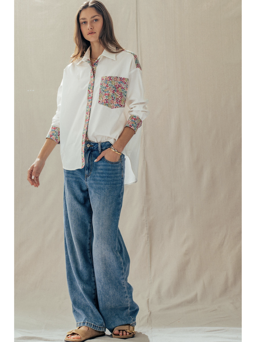 Woman wearing a white shirt with floral patterns and blue jeans against a plain background