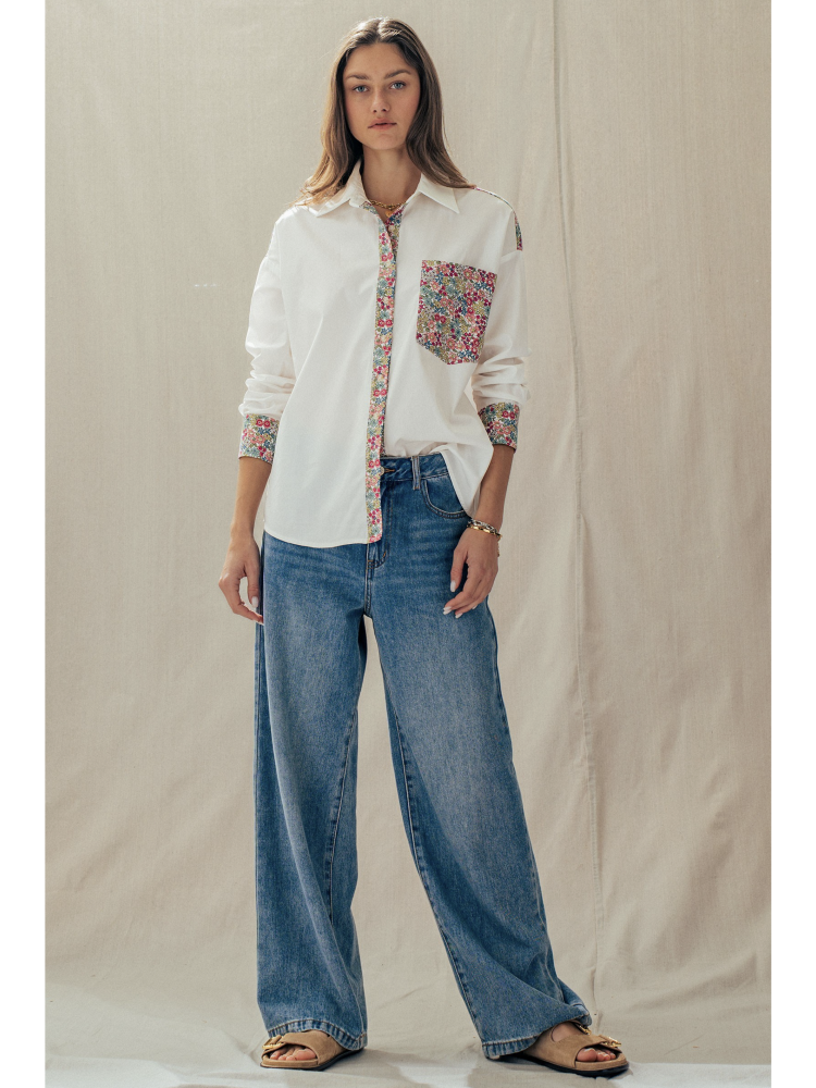 Woman wearing a white shirt with floral patterns and blue jeans against a plain background