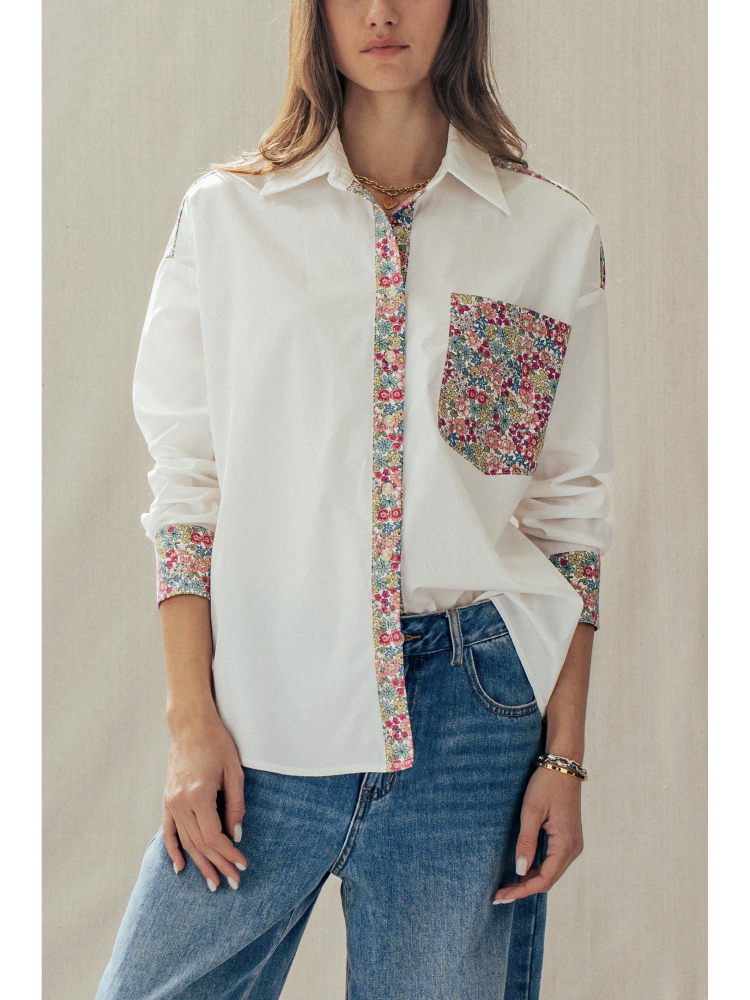 Woman wearing a white shirt with floral patterned sleeves and pocket on a beige background