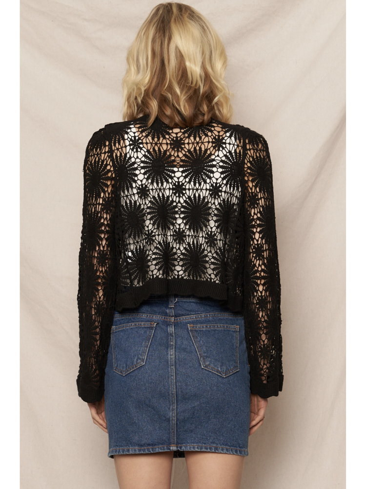 Model wearing a black open-knit crochet cardigan with a floral sunburst pattern, scalloped edges, and long lace sleeves.