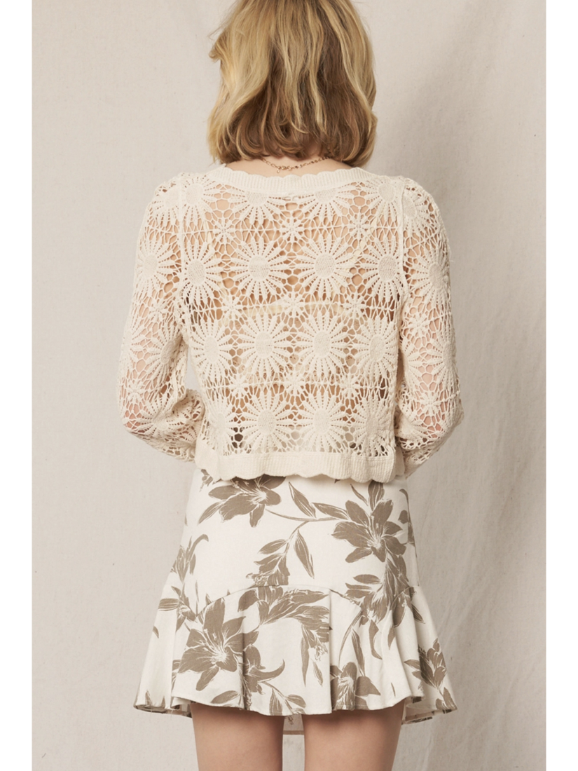 Model wearing a cream open-knit crochet cardigan with a floral sunburst pattern, scalloped edges, and long lace sleeves.