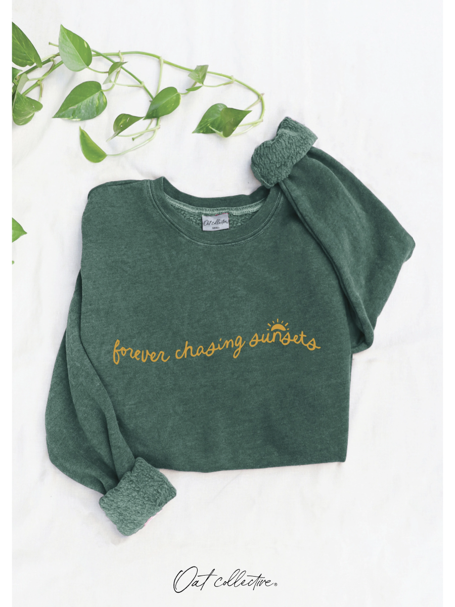 Green sweatshirt with 'forever chasing sunsets' text on a white background with green leaves.