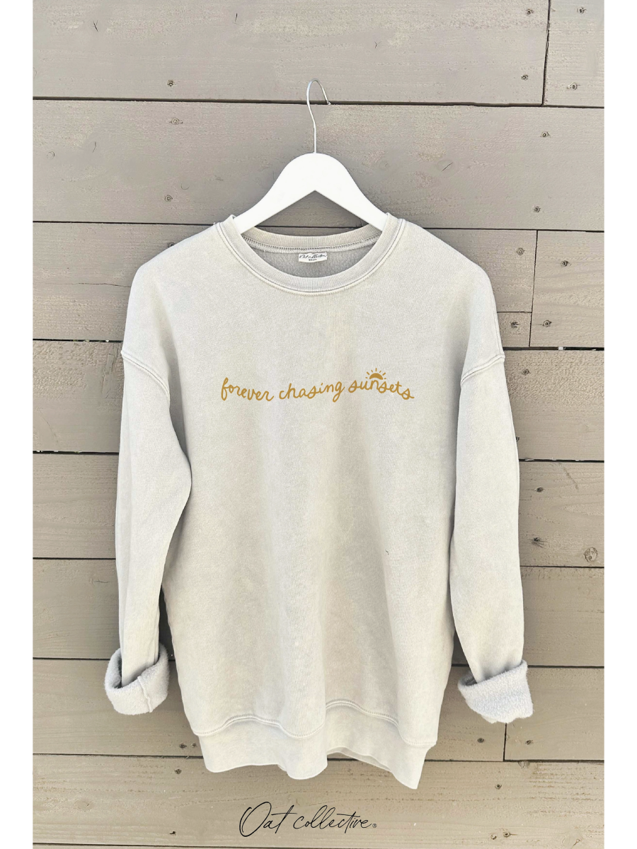 Beige sweatshirt with 'forever chasing sunsets' text on a wooden background