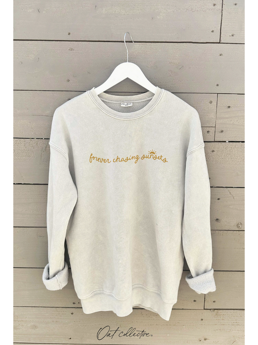 Beige sweatshirt with 'forever chasing sunsets' text on a wooden background