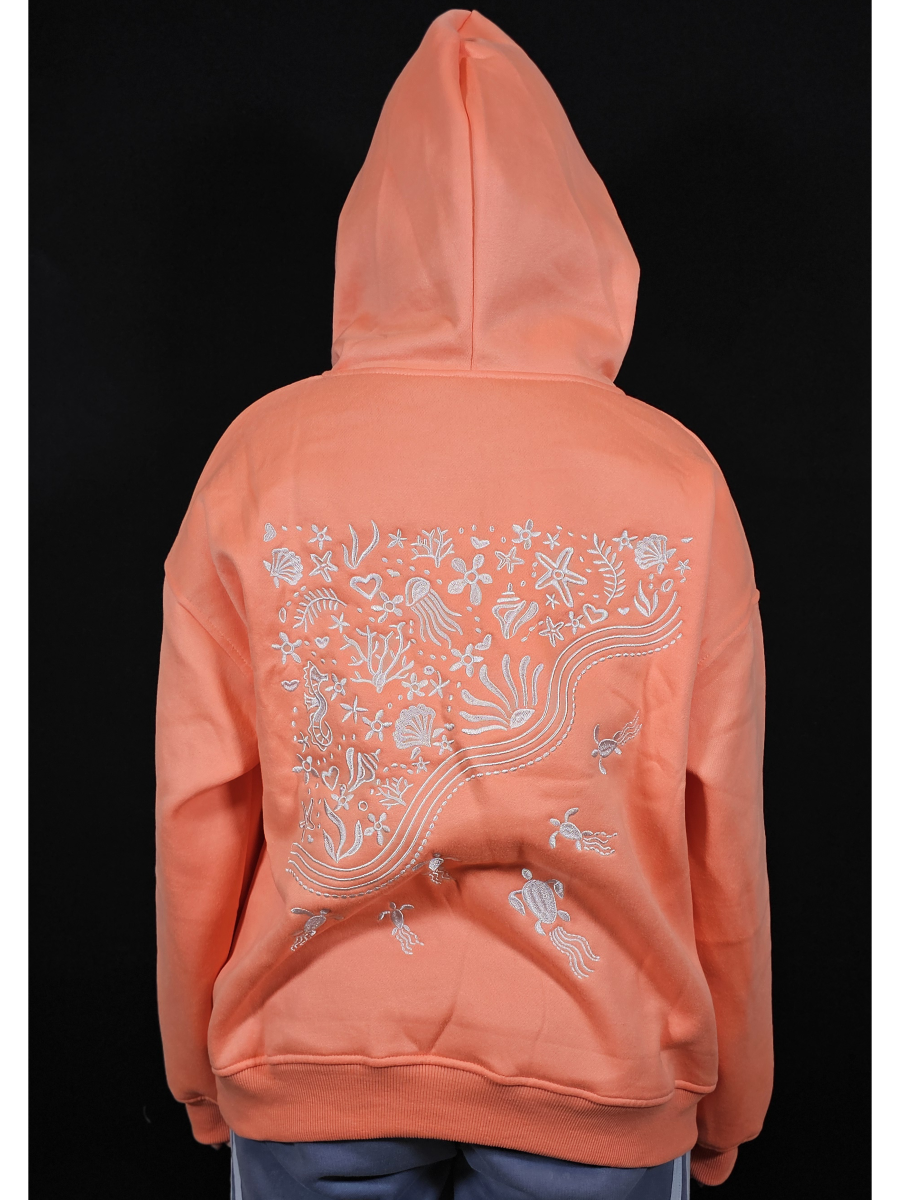 Peach-colored hoodie with embroidered white sea life patterns on the back against a black background
