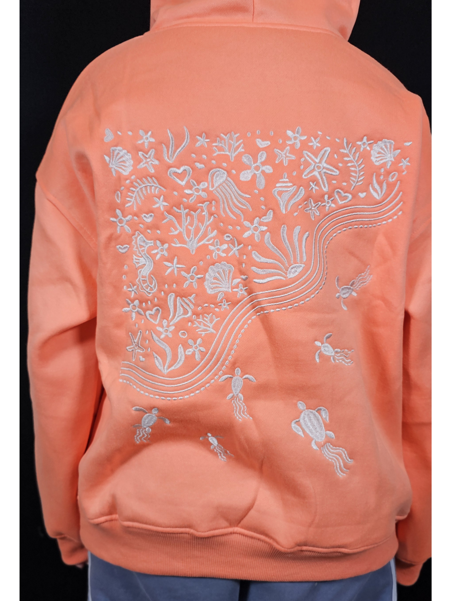 Peach-colored hoodie with white ocean-themed design on the back against a black background