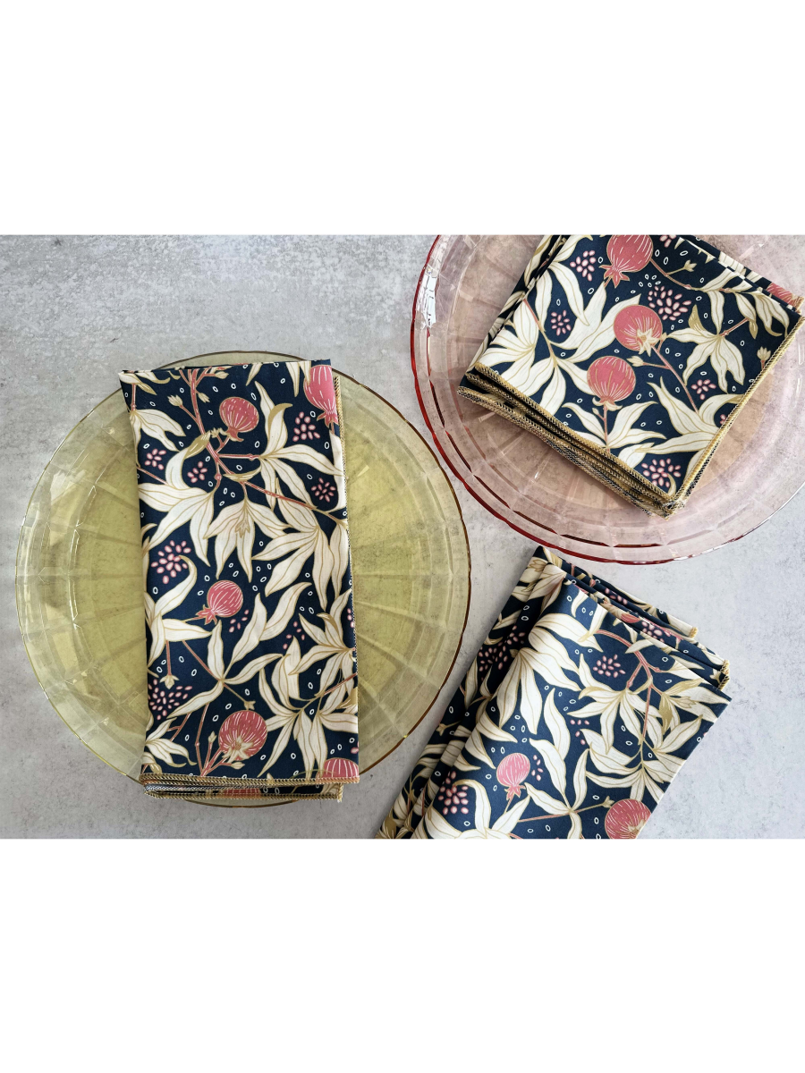 Set of four white cloth napkins featuring a vibrant red gooseberry and green leaf watercolor pattern, folded neatly on a wooden surface.