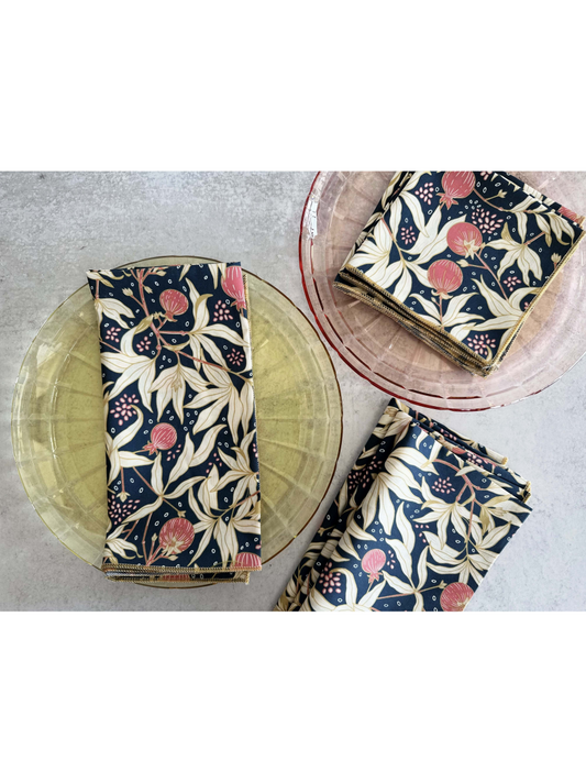 Set of four white cloth napkins featuring a vibrant red gooseberry and green leaf watercolor pattern, folded neatly on a wooden surface.