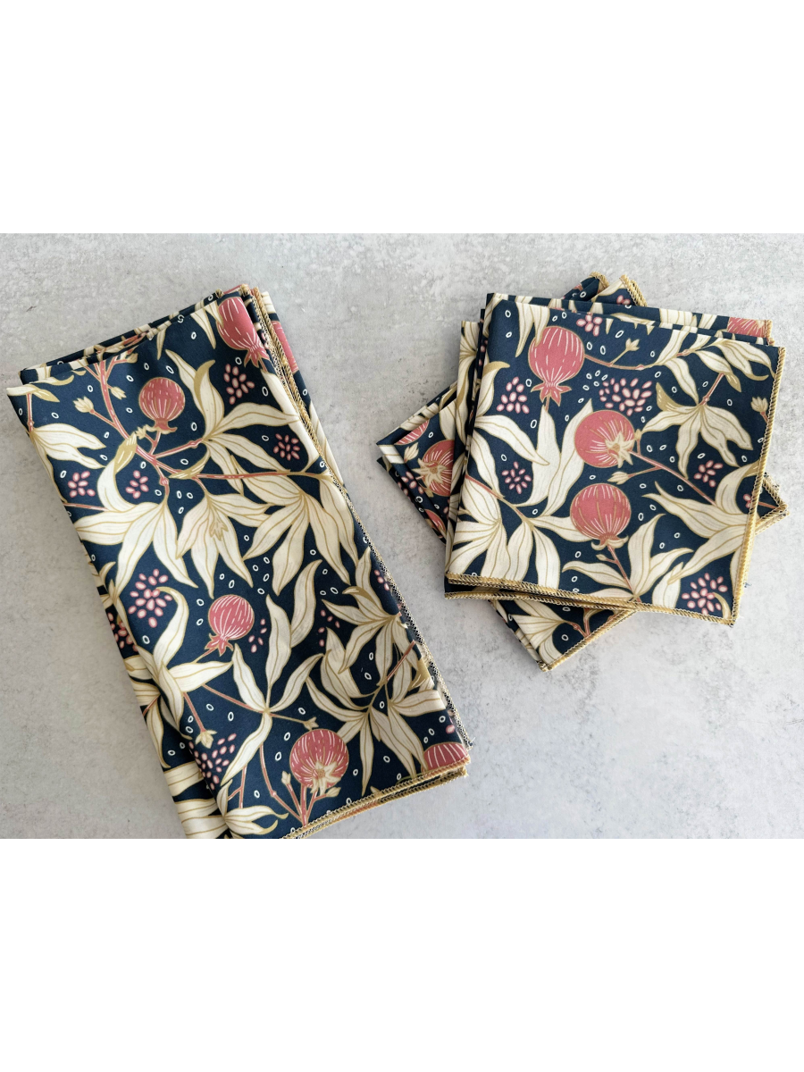 Set of four white cloth napkins featuring a vibrant red gooseberry and green leaf watercolor pattern, folded neatly on a wooden surface.