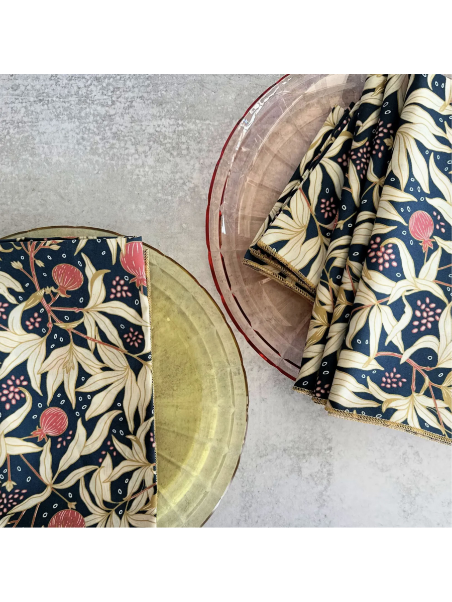 Set of four white cloth napkins featuring a vibrant red gooseberry and green leaf watercolor pattern, folded neatly on a wooden surface.