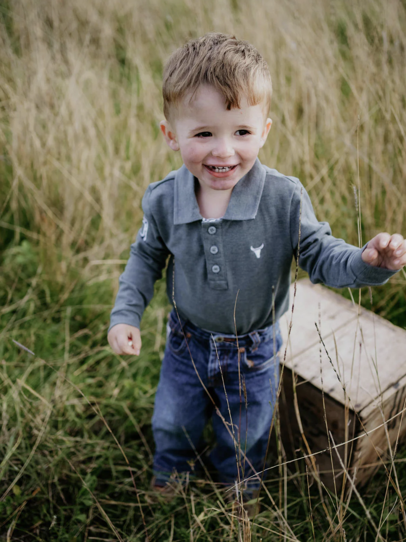 Child in a gray shirt and blue jeans standing in tall grass