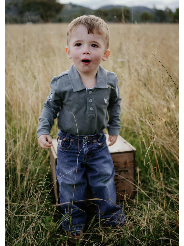 Child in a gray shirt and blue jeans standing in a field with a wooden box.