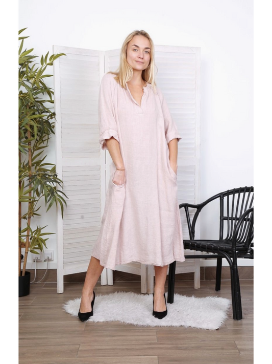 Woman wearing a pink color 100% linen long dress with a V-neck and relaxed fit, standing on a white rug next to a black chair.