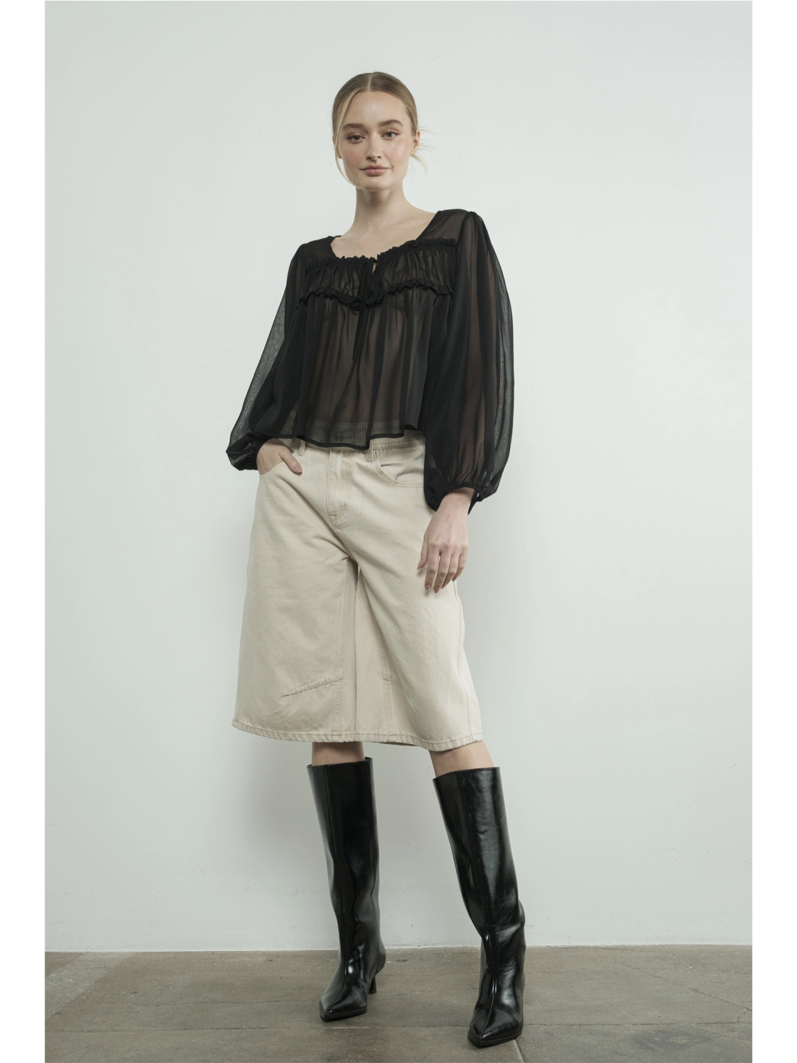 A woman wearing high-waisted cream Bermuda shorts with a yoke seam detail and side pockets, paired with a white top against a neutral background.