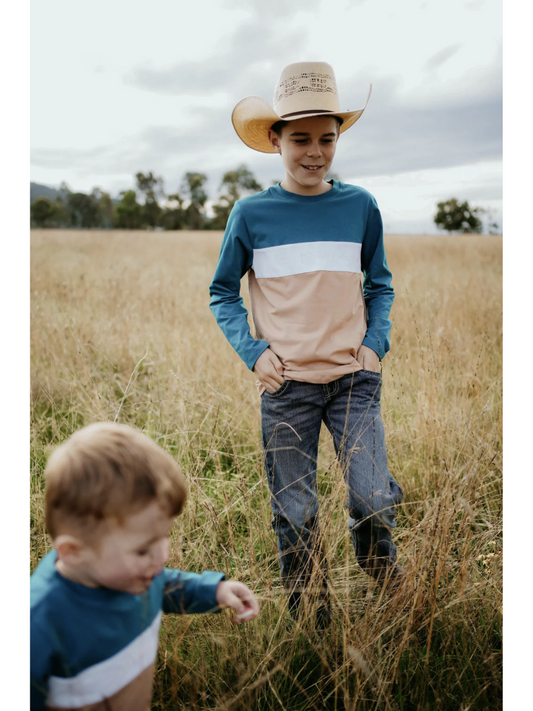Two children in a field with one wearing a cowboy hat and colorful shirt.