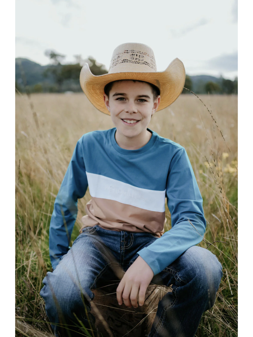 Young boy wearing a cowboy hat and colorful shirt sitting in a field.