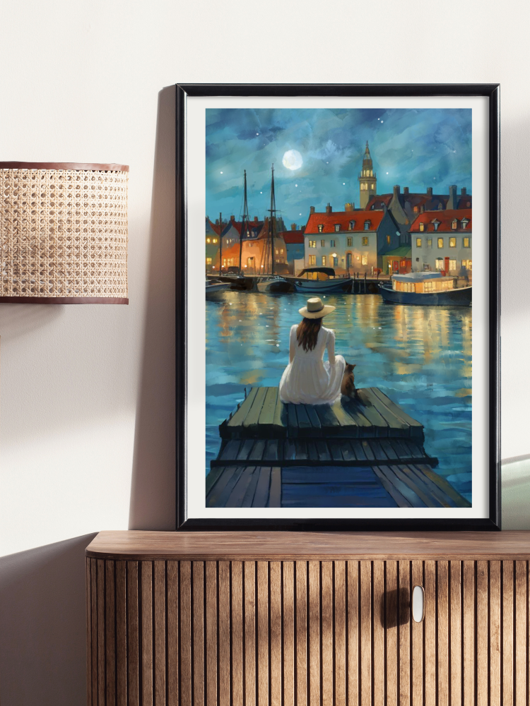 Framed artwork of a woman sitting on a dock by a river with buildings in the background.