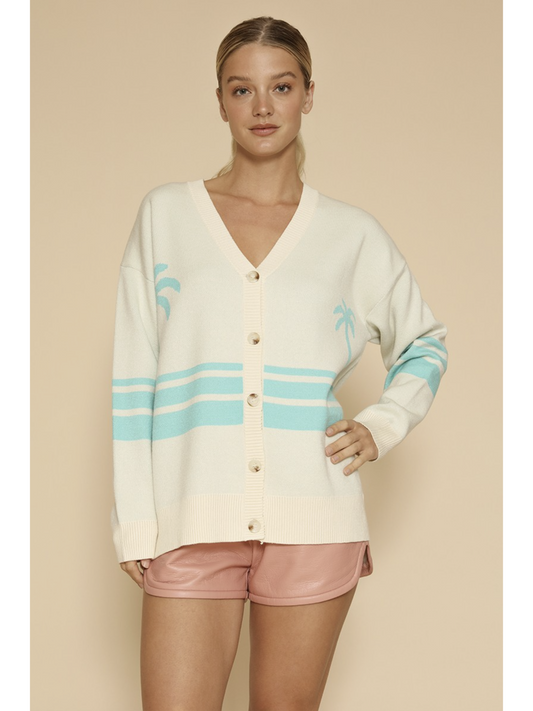 Woman wearing a cream 'coastal themed' cardigan with blue stripes and pink shorts on a beige background
