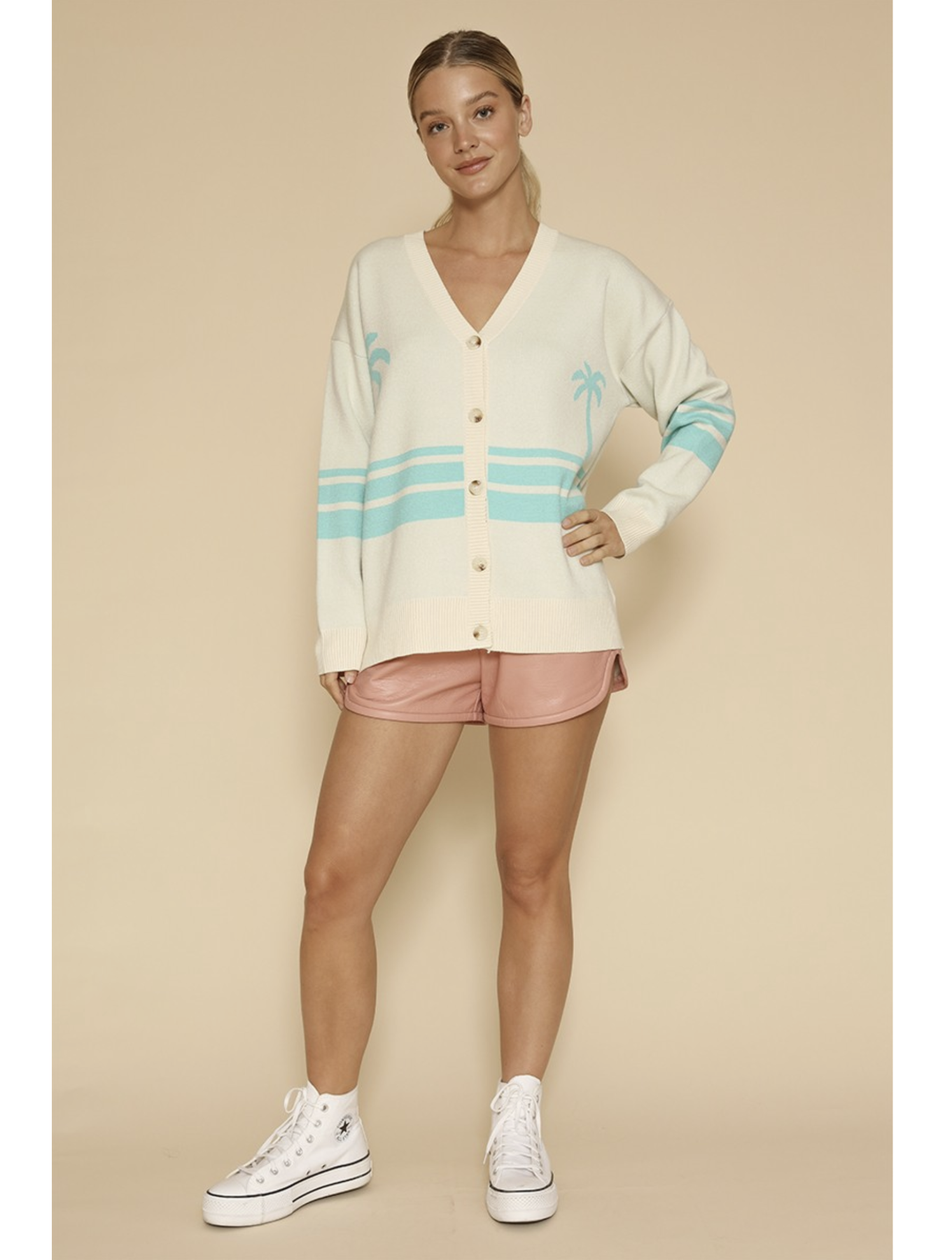 Woman wearing a cream 'coastal theme' cardigan with blue stripes and pink shorts on a beige background