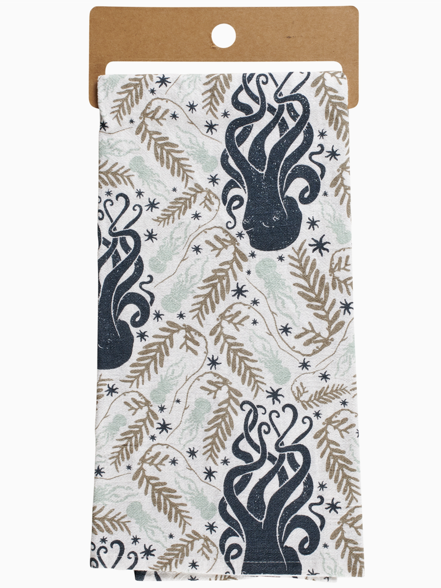 White kitchen towel with a repeating pattern of dark blue octopuses, tan seaweed fronds, and small black stars.