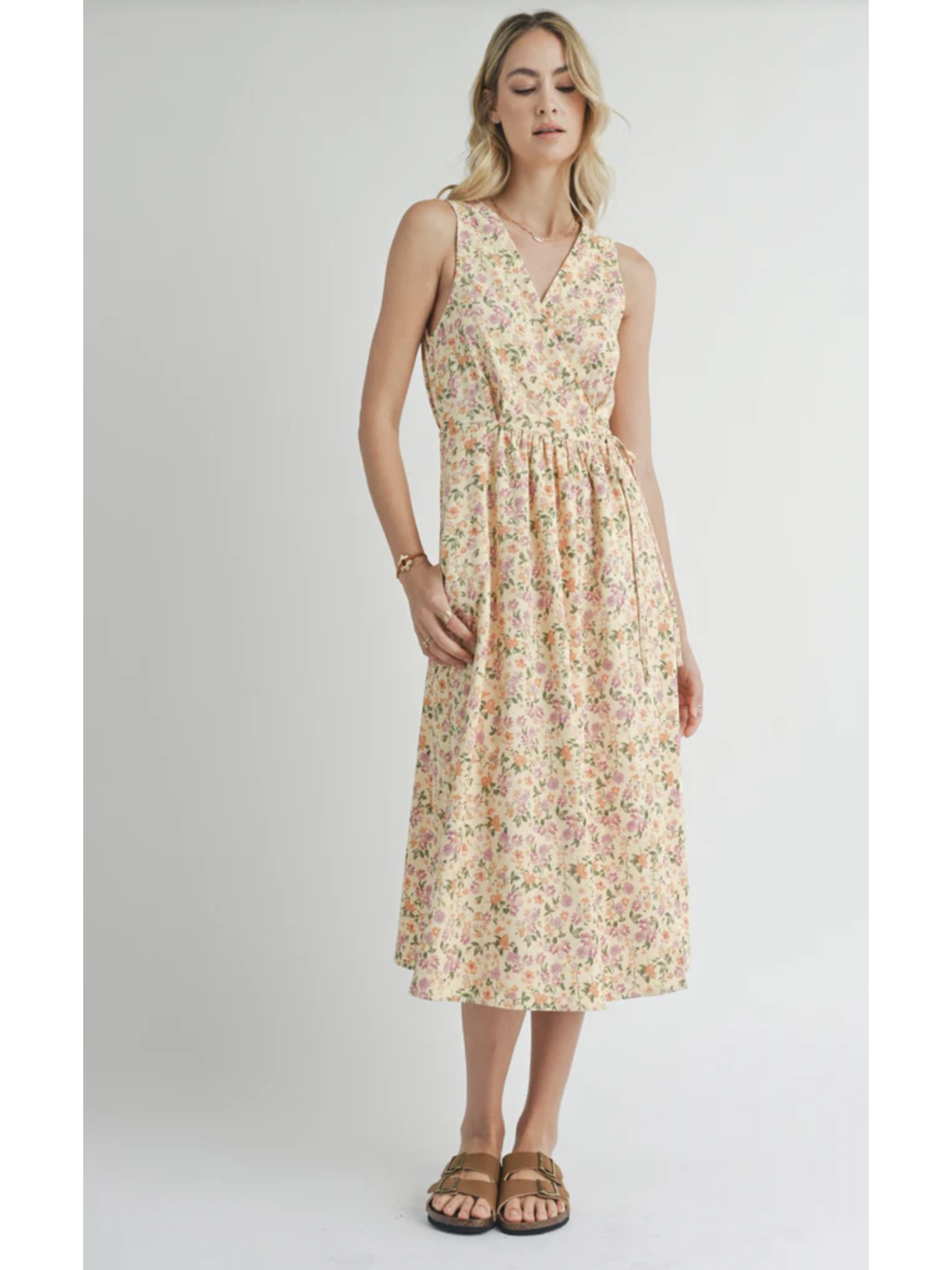 A midi length sleeveless dress with a v-neck design, featuring a floral pattern. The model is wearing the dress with flat sandals.